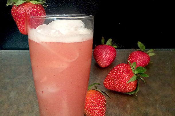 a photo of a glass filled with strawberry drink with whole strawberries beside it