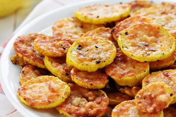 a plate of baked yellow squash rounds covered in baked parmesan cheese