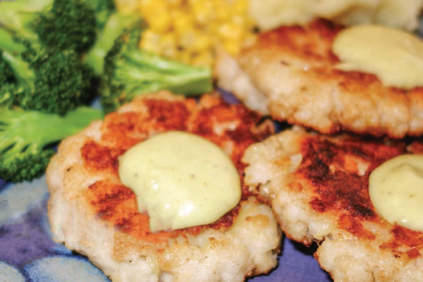 A photo of a plate with 3 fish cakes along side servings of broccoli and corn