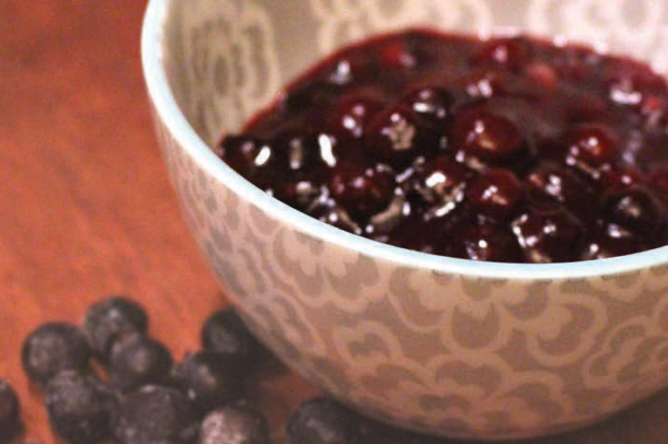 A photo of a bowl of saskatoon berry pudding on a table with a few raw berries beside it