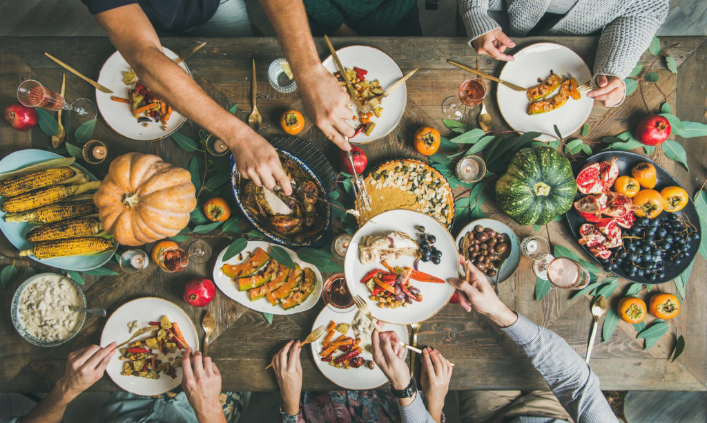 An overview photo of a traditional Thanksgiving dinner table including with turkey, pumpkin pie, roasted seasonal vegetables and fruit