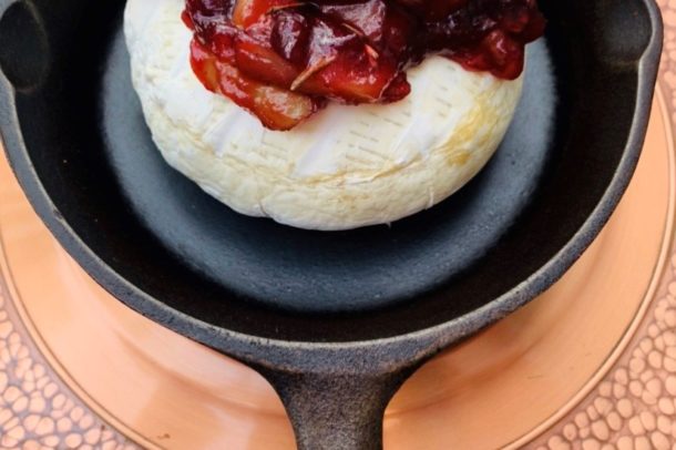 Image of a cast iron frying pan with a round of brie cheese topped with cranberry sauce