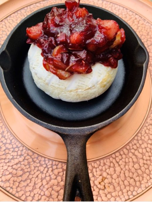 Image of a cast iron frying pan with a round of brie cheese topped with cranberry sauce