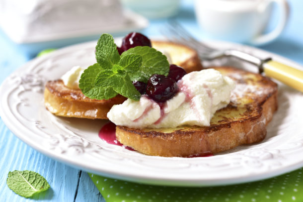 A plate showing 2 pieces of french toast with ricotta cheese, fruits and a basil garnish