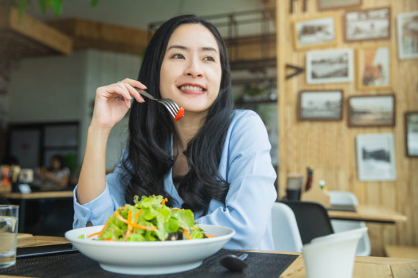 Happy woman eating healthy salad sitting on the table