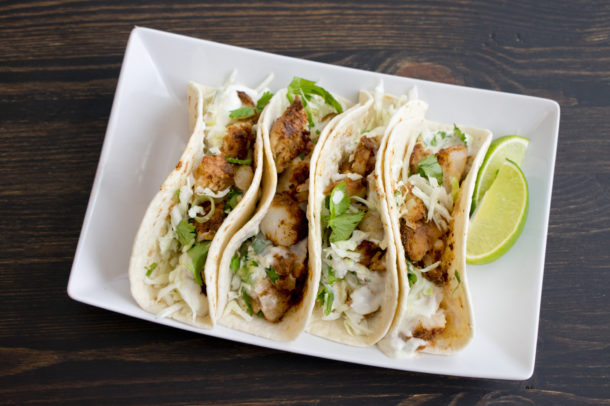 a plate with four fish tacos and a lime wedge