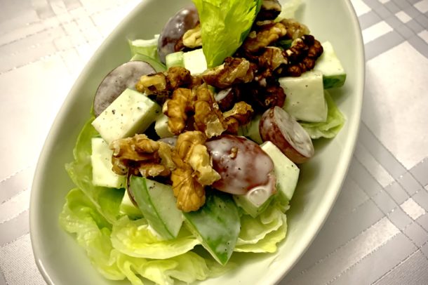 A bowl filled with lettuce greens, topped with whalmuts and applie pieces