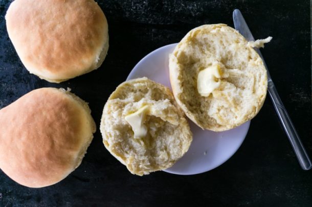 2 dinner rolls next to a plate with a buttered split roll