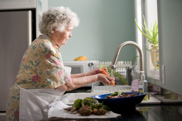 elderly woman washing vegetables at her kitchen sink