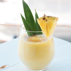 a glass of a tropical cocktail garnished with pineapple and pineapple leaf