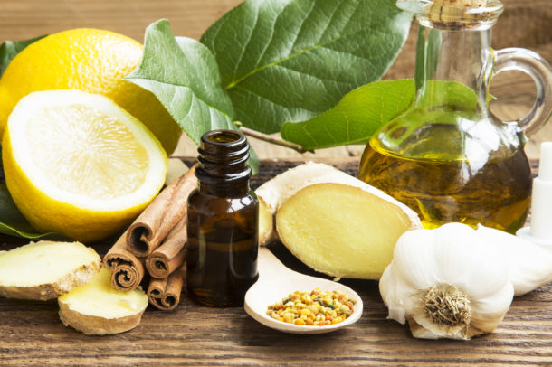 Lemons, ginger slices, garlic and oil surrounding spoons with spices and bottles of oil