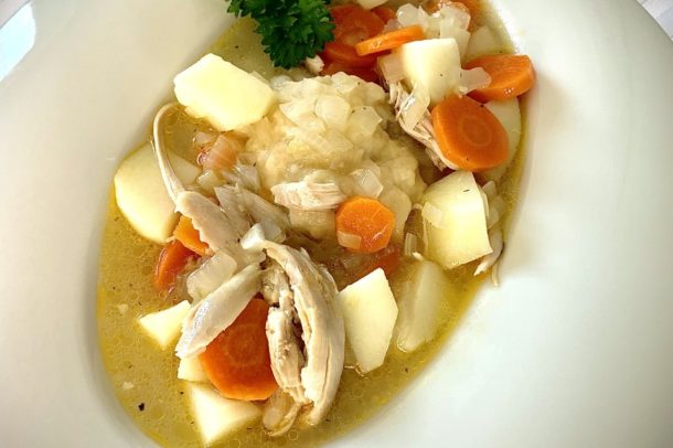 a bowl filled with a traditional Acadian chicken stew including chunks of potato, carrot, chicken and a dumpling in broth