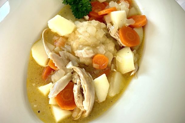 a bowl filled with a traditional Acadian chicken stew including chunks of potato, carrot, chicken and a dumpling in broth