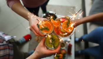 Young group friends hold in hand fruit cocktail with sparkler decoration. Christmas invite party concept. Heath care vegan summer drinks