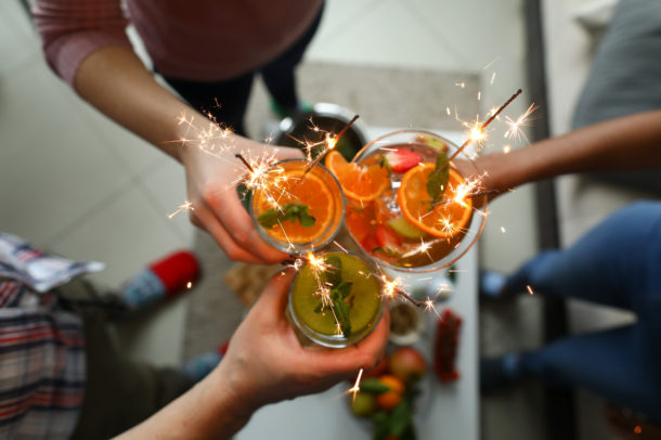 Young group friends hold in hand fruit cocktail with sparkler decoration. Christmas invite party concept. Heath care vegan summer drinks