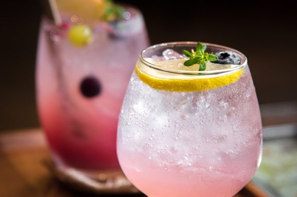 two cocktails glasses filled with ice and pink beverage with lemon garnish