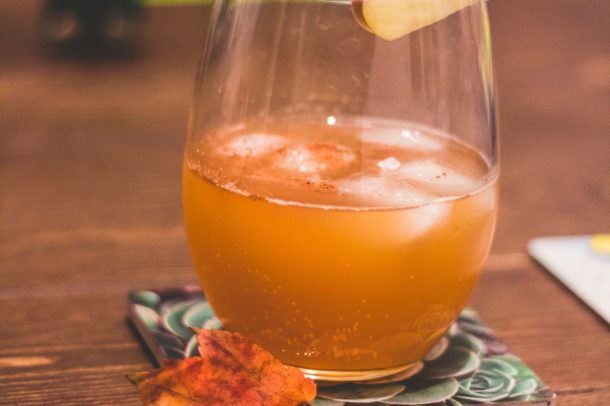 a cocktail glass on a coaster with a apple based liquid and apple wedge on the glass