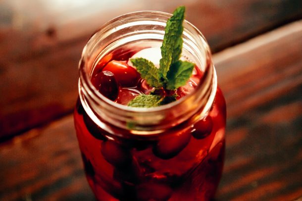 a small mason jar filled with a red liquid garnished with cranberries and mind