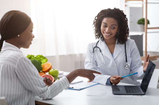 Personal nutrition plan. African american woman dietologist consulting patient, using laptop, clinic interior