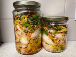 two jars, one larger than the other, filled with fermented cabbage, onions and chili flakes - kimchi