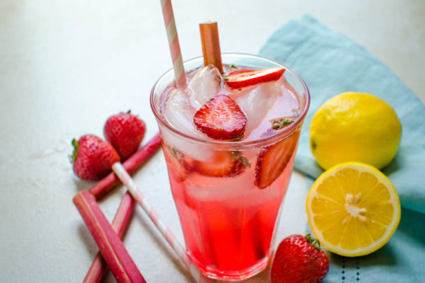 a clear glass filled with pink liquid, ice cubes a stalk of rhubarb and a straw