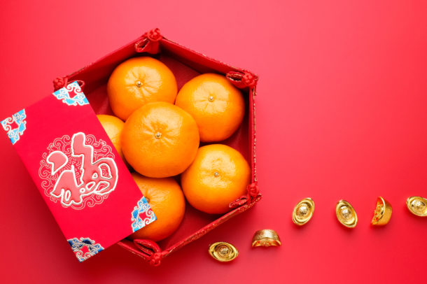 Group of orange tangerine in Chinese pattern tray and envelope packet ang pow with gold ingots on red table top. Chinese new year concep.Chinese Language on envelop is happiness,on ingot is wealthy