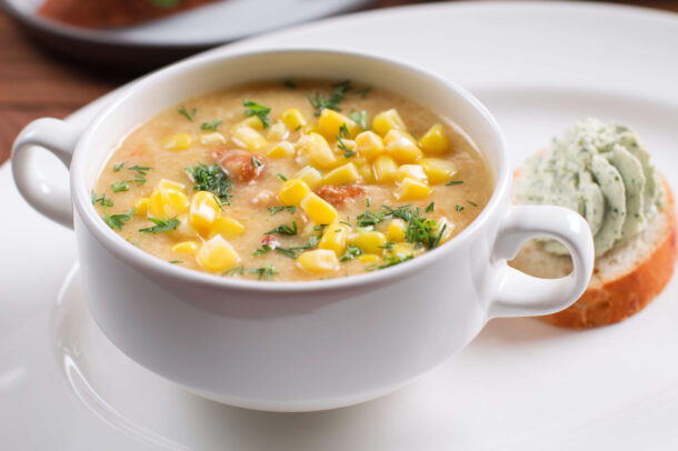 chicken Chili stew topped with herbs, served in a white bowl with bread and spread.