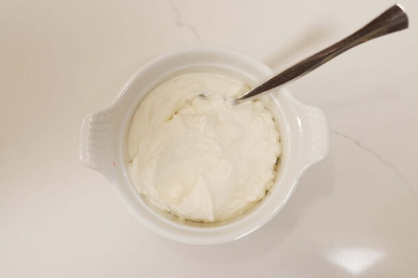 Bowl of whipped crème fraîche with a spoon on a white countertop.