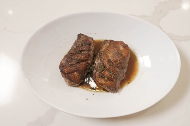 Seared duck breast sliced into thick pieces and served on a white plate with pan sauce and herbs.