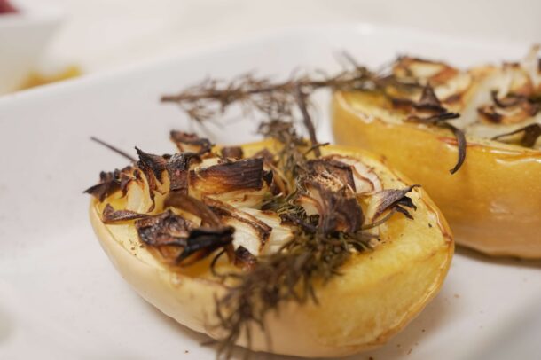 Roasted spaghetti squash halves topped with caramelized onions and fresh thyme on a white plate.