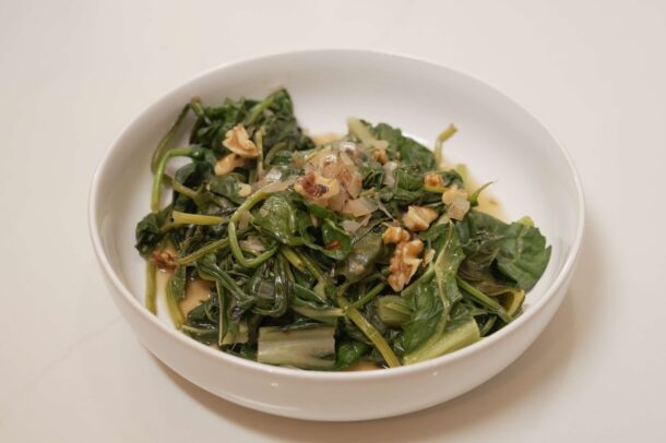 Bowl of wilted leafy greens sautéed with onions and topped with chopped nuts in a light sauce.