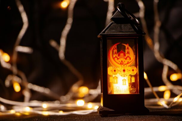 Ramadan lantern on a table with decorative lights in the background.
