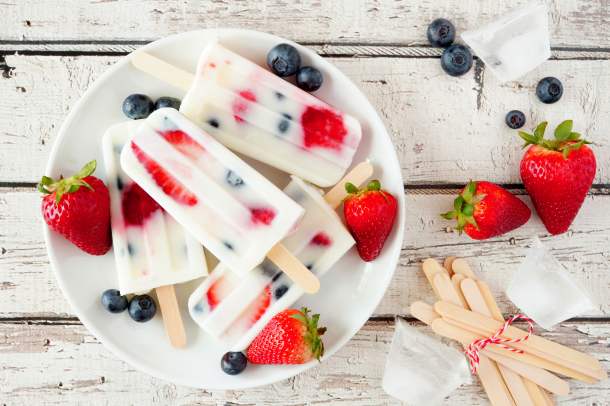 Sucettes glacées aux petits fruits et au yogourt, garnies de fraises et de bleuets frais, présentées sur une assiette blanche.